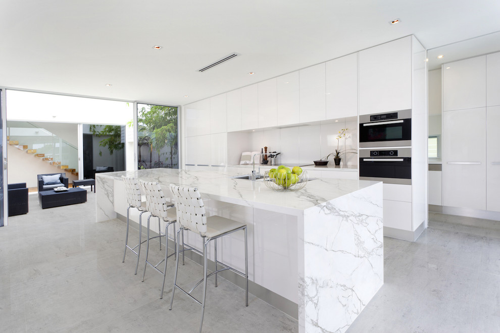 Inspiration for a contemporary galley kitchen remodel in Miami with flat-panel cabinets, white cabinets, white backsplash, stainless steel appliances, an island and a double-bowl sink