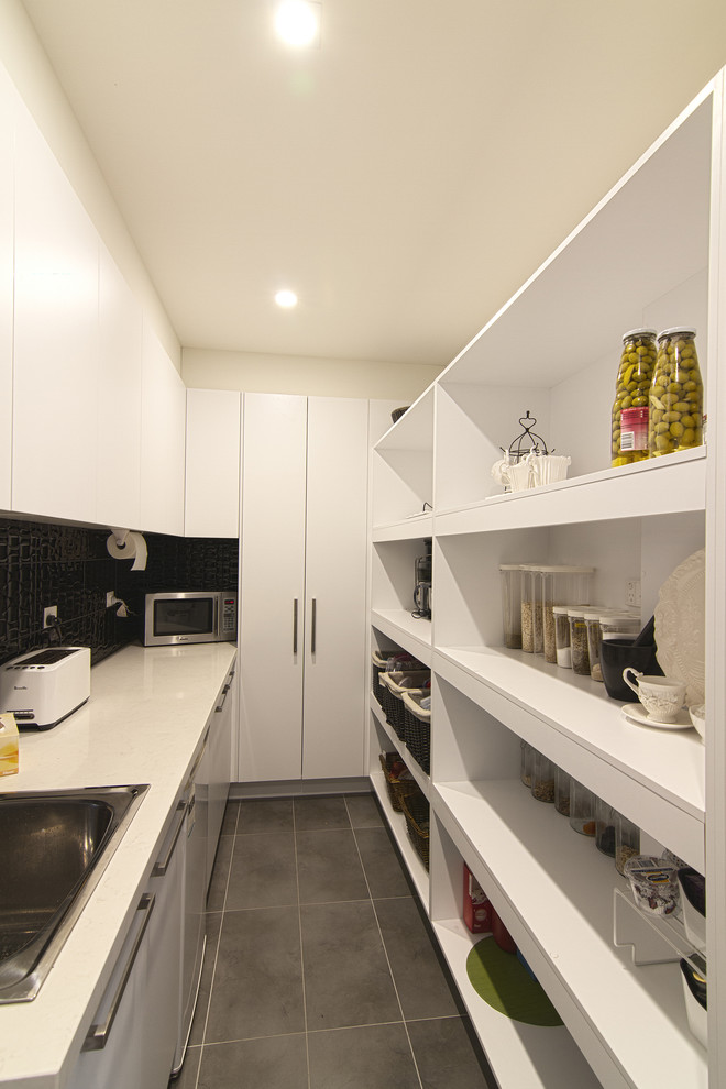 Inspiration for a large modern l-shaped kitchen pantry in Melbourne with a built-in sink, flat-panel cabinets, white cabinets, engineered stone countertops, black splashback, porcelain splashback, stainless steel appliances and porcelain flooring.