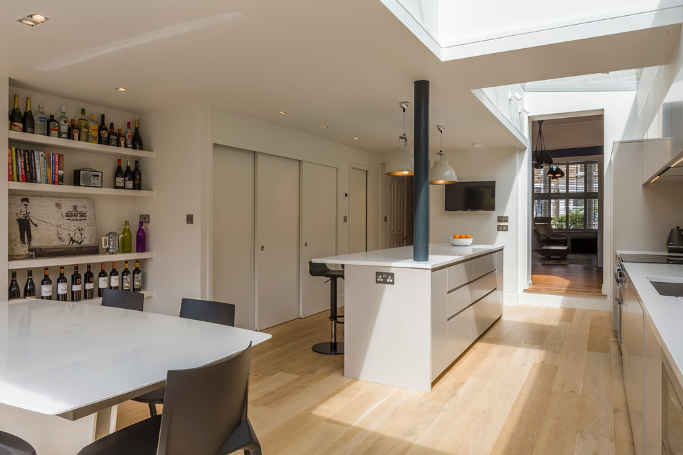 Example of a trendy light wood floor eat-in kitchen design in London with an island, flat-panel cabinets, gray cabinets, solid surface countertops, stainless steel appliances and a double-bowl sink