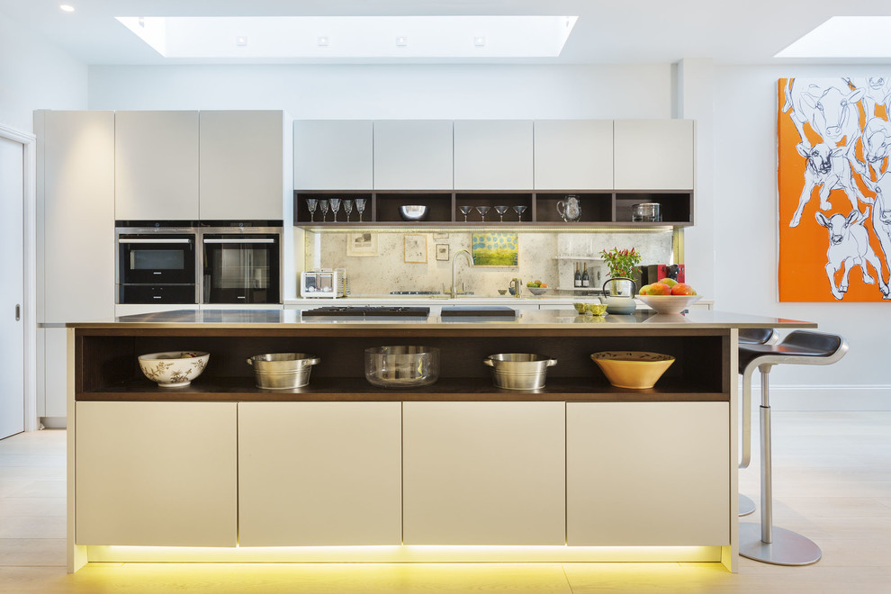 Photo of a large modern single-wall open plan kitchen in London with flat-panel cabinets, white cabinets, light hardwood flooring and an island.