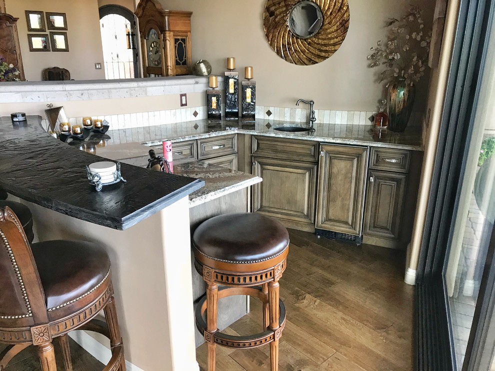 Example of a large mountain style single-wall travertine floor and beige floor open concept kitchen design in Phoenix with an undermount sink, raised-panel cabinets, brown cabinets, beige backsplash, travertine backsplash, stainless steel appliances, two islands, beige countertops and granite countertops