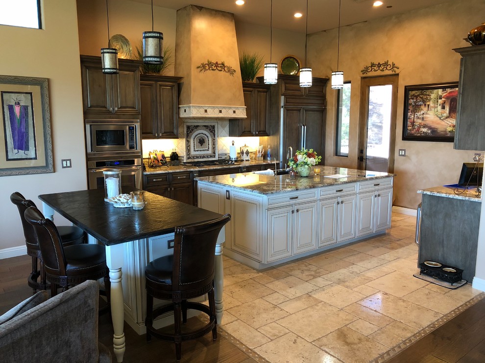 Photo of a large rustic single-wall open plan kitchen in Phoenix with a submerged sink, raised-panel cabinets, brown cabinets, beige splashback, travertine splashback, stainless steel appliances, travertine flooring, multiple islands, beige floors, beige worktops and granite worktops.