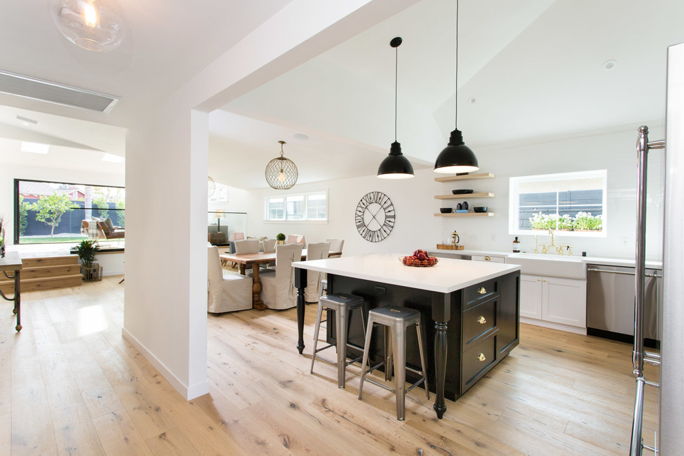 Example of a cottage light wood floor open concept kitchen design in Los Angeles with a farmhouse sink, shaker cabinets, white cabinets, quartzite countertops, stainless steel appliances and an island