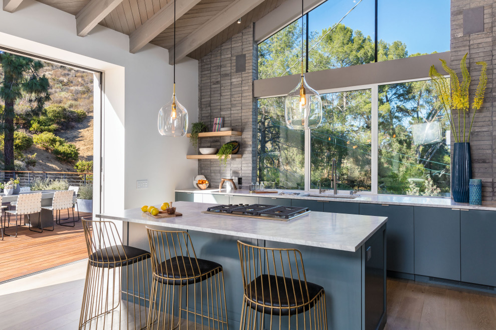 Moderne Küche mit Unterbauwaschbecken, flächenbündigen Schrankfronten, blauen Schränken, Rückwand-Fenster, hellem Holzboden, Kücheninsel und weißer Arbeitsplatte in Los Angeles