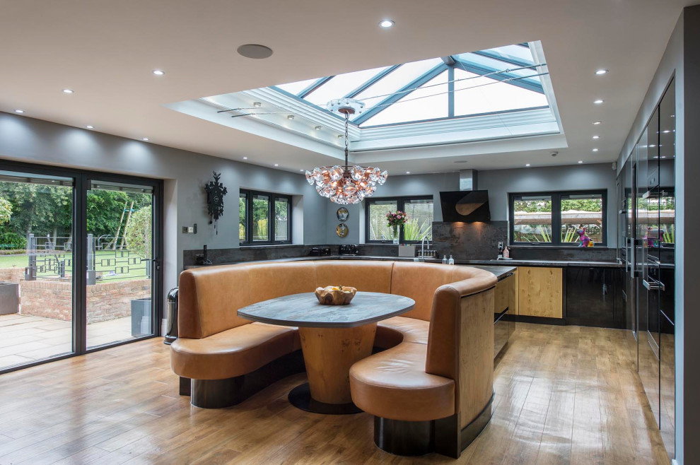 Large contemporary u-shaped open plan kitchen in Other with a submerged sink, flat-panel cabinets, black cabinets, engineered stone countertops, multi-coloured splashback, stone slab splashback, stainless steel appliances, medium hardwood flooring, an island, brown floors and multicoloured worktops.