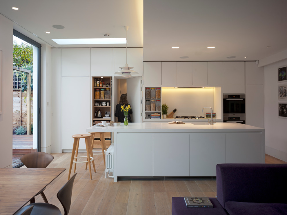 Einzeilige Moderne Wohnküche mit integriertem Waschbecken, flächenbündigen Schrankfronten, weißen Schränken, Mineralwerkstoff-Arbeitsplatte und Kücheninsel in London