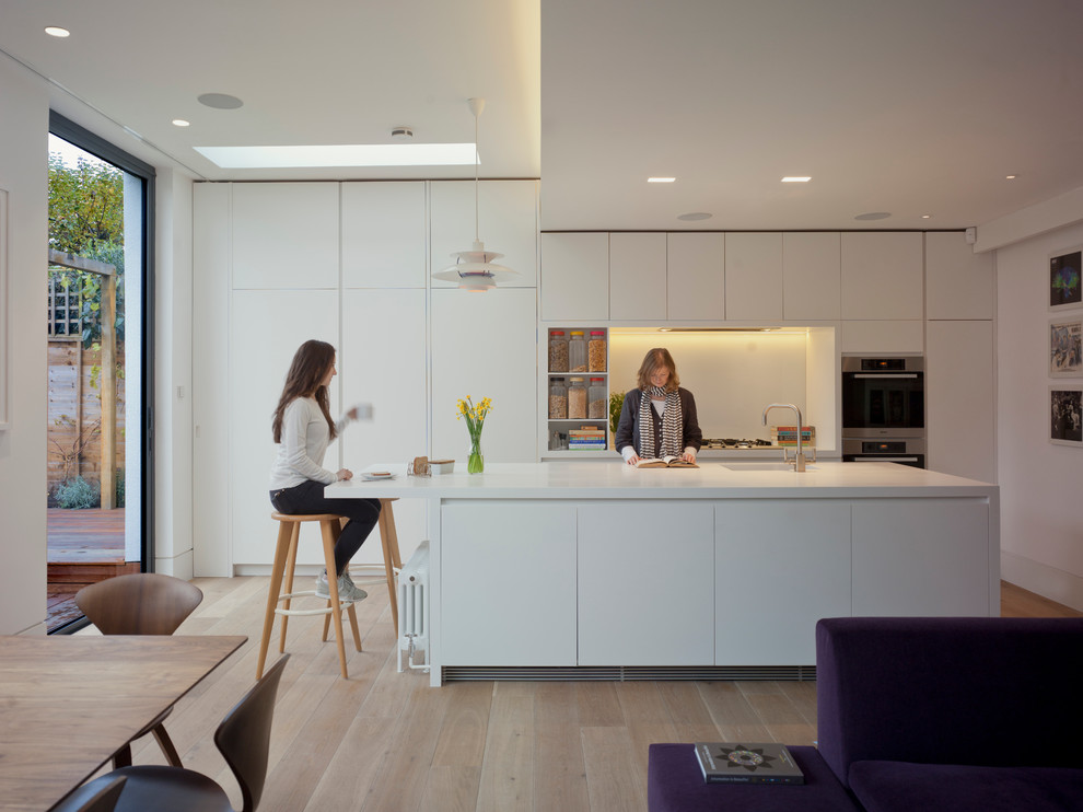 Example of a trendy single-wall kitchen design in London with an integrated sink, flat-panel cabinets, white cabinets, solid surface countertops and an island