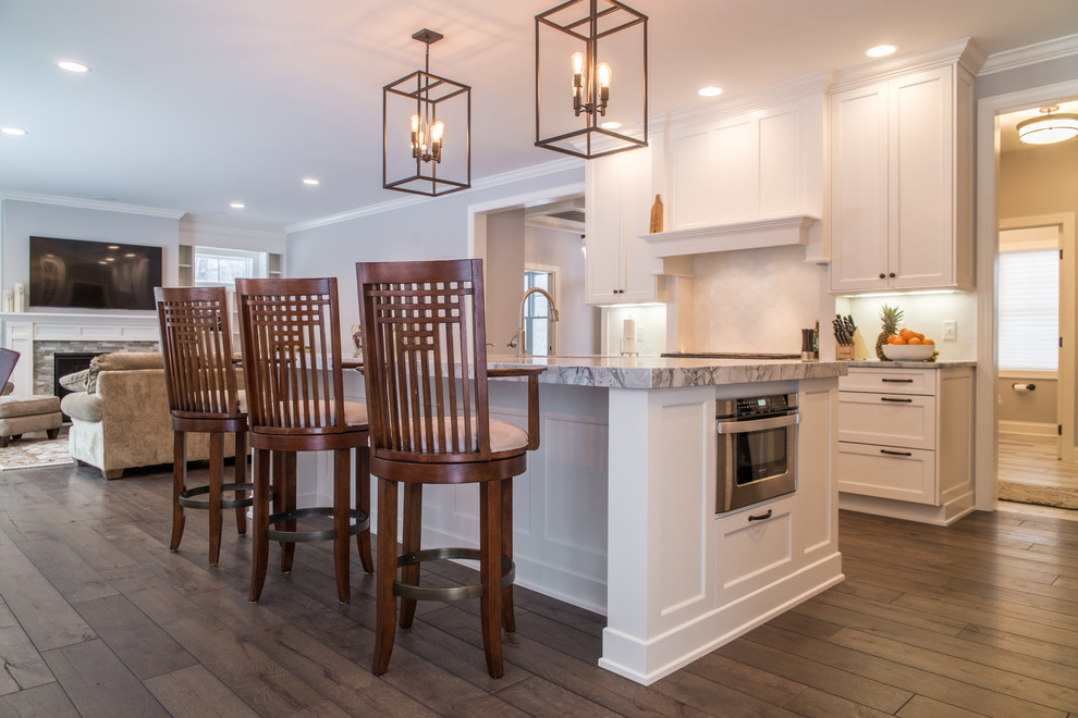 Foto på ett stort amerikanskt kök, med vita skåp, rostfria vitvaror, mörkt trägolv, en köksö, en undermonterad diskho och brunt golv