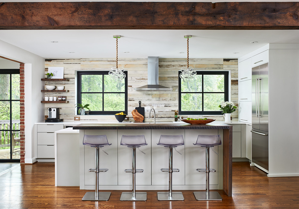 Modelo de cocina contemporánea con armarios con paneles lisos, salpicadero de madera, electrodomésticos de acero inoxidable, suelo de madera en tonos medios y una isla