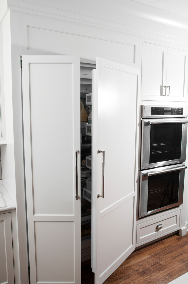 Exempel på ett stort amerikanskt kök, med en undermonterad diskho, skåp i shakerstil, vita skåp, bänkskiva i kvartsit, grått stänkskydd, stänkskydd i tunnelbanekakel, integrerade vitvaror, mellanmörkt trägolv, en köksö och brunt golv