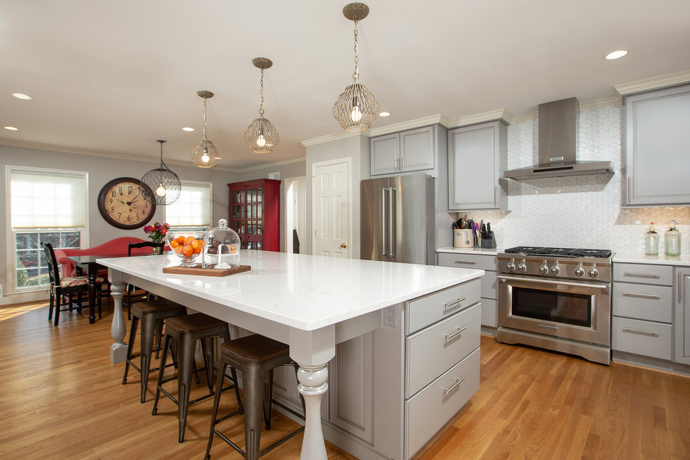 Foto på ett vintage vit kök och matrum, med luckor med upphöjd panel, grå skåp, vitt stänkskydd, rostfria vitvaror, en köksö och ljust trägolv