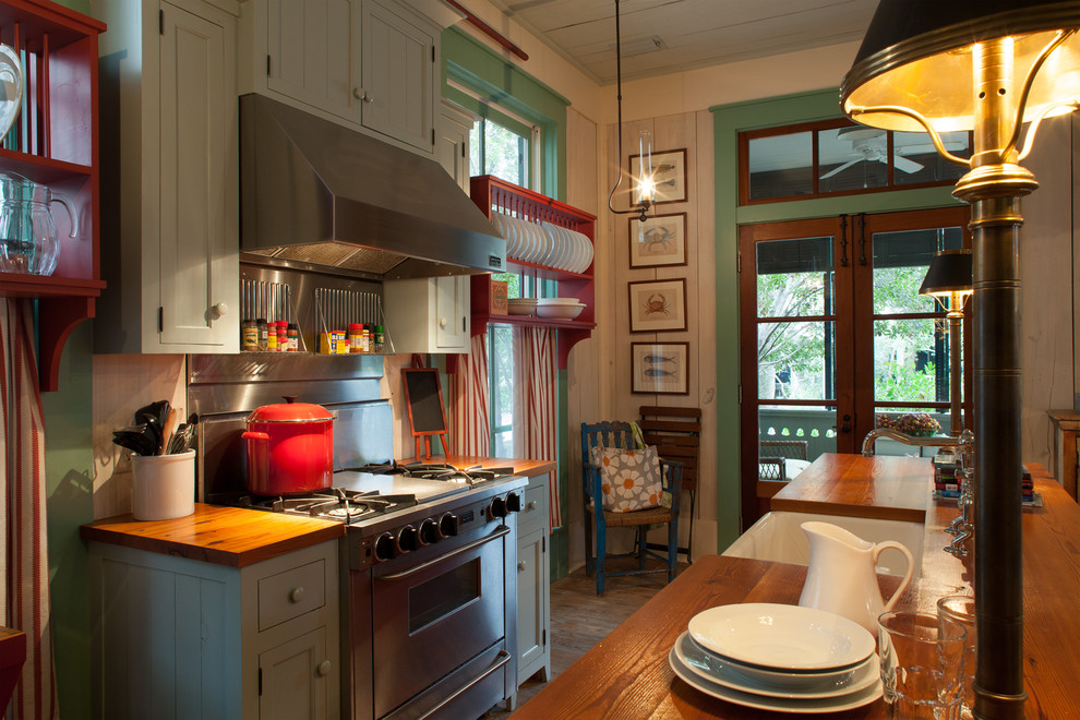 Ejemplo de cocina costera con electrodomésticos de acero inoxidable, encimera de madera, armarios con paneles empotrados y puertas de armario verdes