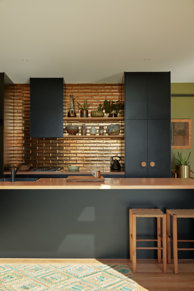 На фото: параллельная кухня в современном стиле с накладной мойкой, плоскими фасадами, черными фасадами, фартуком цвета металлик, паркетным полом среднего тона, островом, коричневым полом, бежевой столешницей и красивой плиткой с
