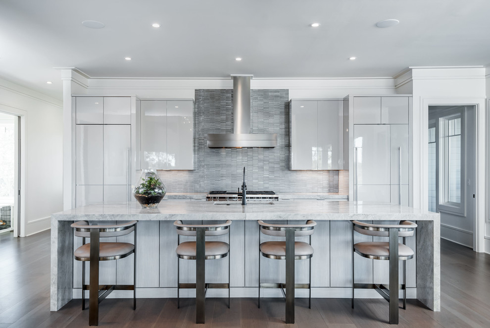 Example of a trendy galley medium tone wood floor and brown floor open concept kitchen design in Charleston with an undermount sink, flat-panel cabinets, gray backsplash, an island, gray countertops, beige cabinets, marble countertops, metal backsplash and paneled appliances