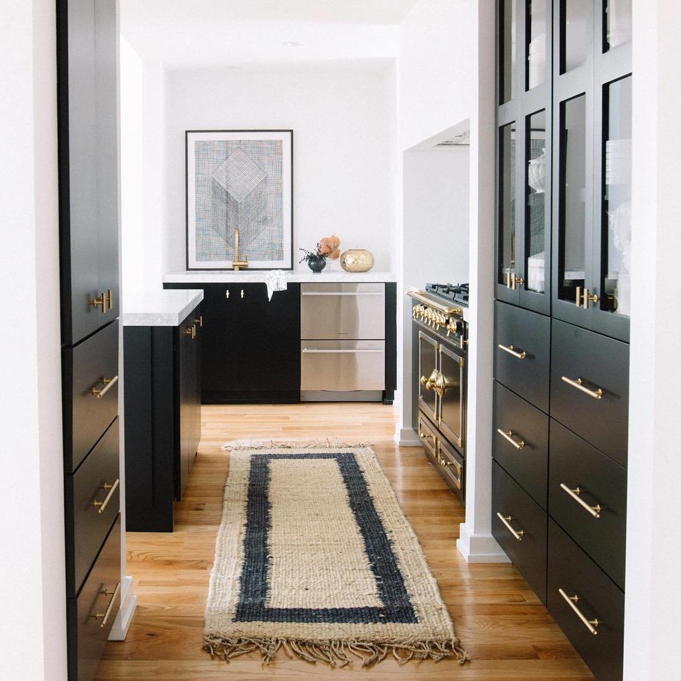 Foto di un grande cucina con isola centrale minimal con ante lisce, ante nere, top in marmo, pavimento in legno massello medio, pavimento marrone e top bianco