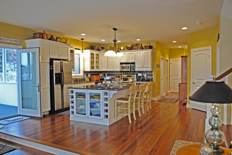 Large beach style l-shaped medium tone wood floor open concept kitchen photo in Grand Rapids with a double-bowl sink, beaded inset cabinets, yellow cabinets, granite countertops, gray backsplash, glass tile backsplash, stainless steel appliances and an island
