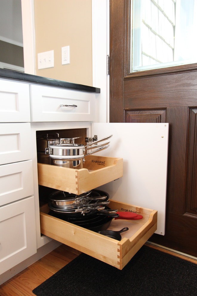 Klassisk inredning av ett avskilt, litet l-kök, med en undermonterad diskho, skåp i shakerstil, vita skåp, bänkskiva i kvarts, vitt stänkskydd, stänkskydd i tunnelbanekakel, rostfria vitvaror, mellanmörkt trägolv och en halv köksö