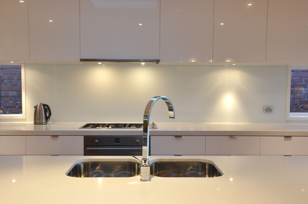 Exempel på ett mellanstort modernt kök, med en undermonterad diskho, släta luckor, vita skåp, bänkskiva i kvarts, vitt stänkskydd, glaspanel som stänkskydd, rostfria vitvaror, ljust trägolv och en köksö