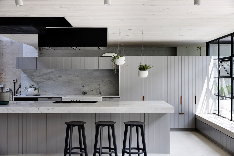 Cette image montre une cuisine ouverte parallèle design avec un évier de ferme, un placard à porte plane, des portes de placard grises, une crédence grise, îlot et un sol beige.