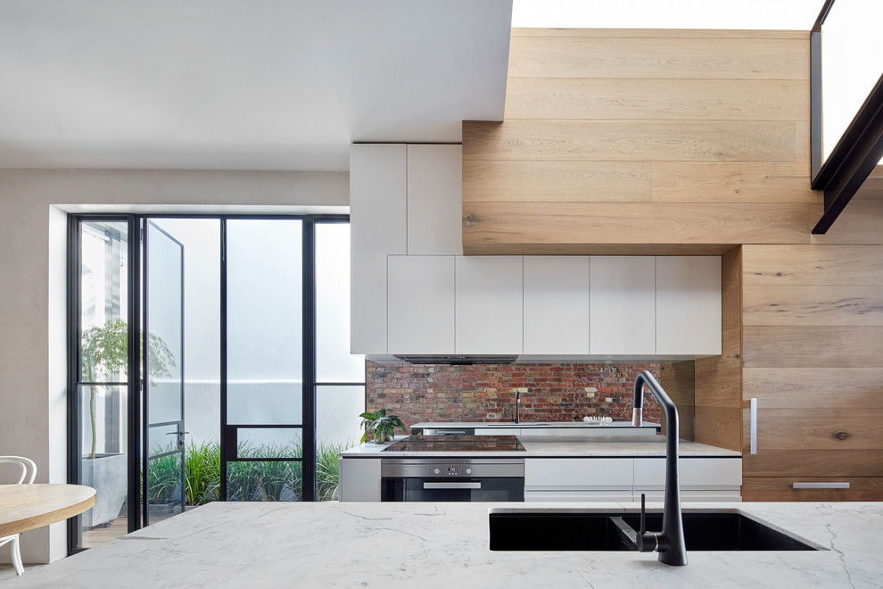 Idéer för ett litet modernt kök, med en undermonterad diskho, släta luckor, skåp i ljust trä, marmorbänkskiva, spegel som stänkskydd, svarta vitvaror, betonggolv, en köksö och grått golv