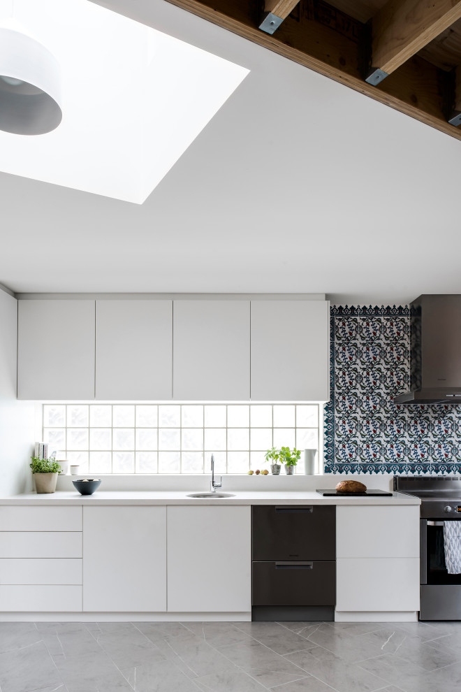 Foto på ett mellanstort funkis vit l-kök, med en undermonterad diskho, släta luckor, vita skåp, stänkskydd i travertin, rostfria vitvaror och grått golv