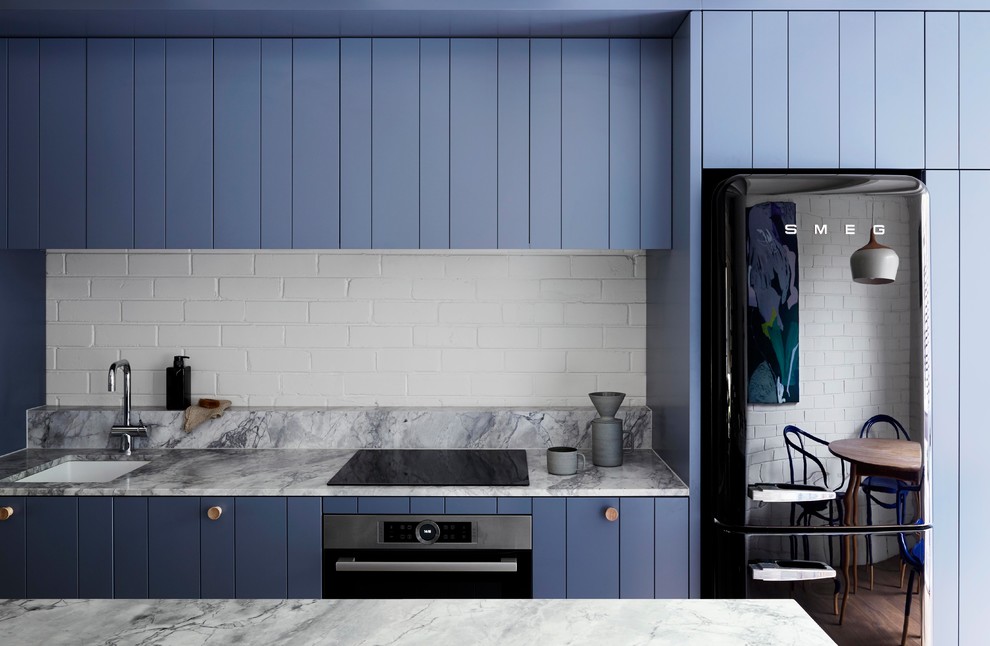 Inredning av ett modernt litet grå grått kök, med en undermonterad diskho, blå skåp, bänkskiva i kvartsit, vitt stänkskydd, stänkskydd i tegel, svarta vitvaror, mellanmörkt trägolv, en köksö, grått golv och släta luckor