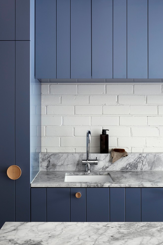 Exempel på ett litet modernt kök, med en undermonterad diskho, luckor med infälld panel, blå skåp, bänkskiva i kvartsit, vitt stänkskydd, stänkskydd i tegel, svarta vitvaror, mellanmörkt trägolv, en köksö och grått golv