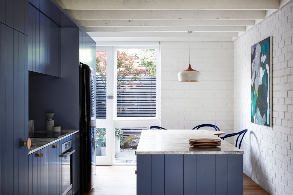 Inredning av ett modernt litet kök, med en undermonterad diskho, luckor med infälld panel, blå skåp, bänkskiva i kvartsit, vitt stänkskydd, stänkskydd i tegel, svarta vitvaror, mellanmörkt trägolv, en köksö och grått golv