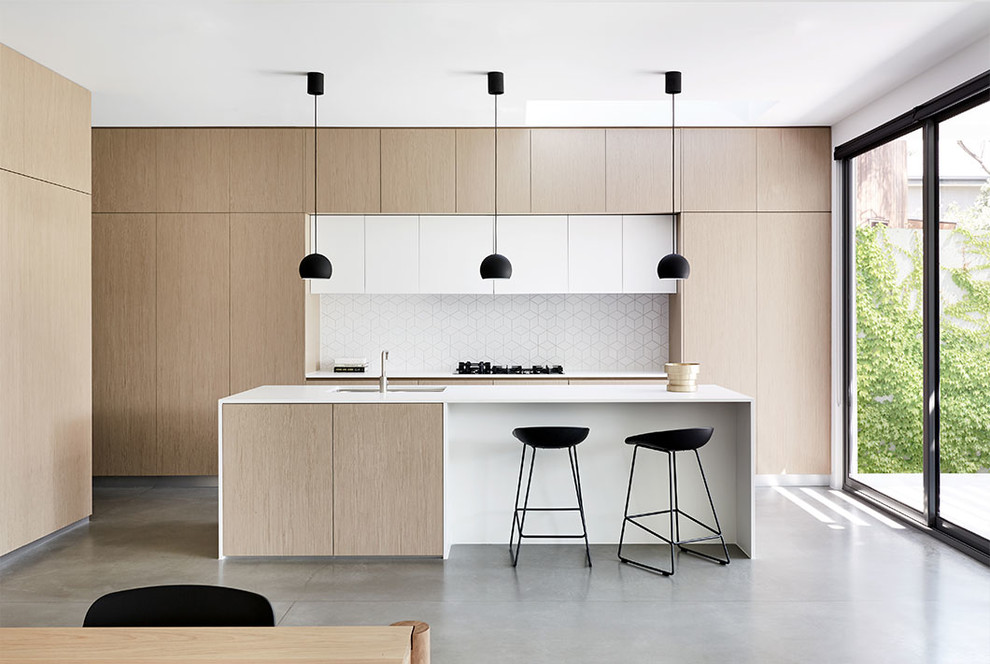 Modern inredning av ett kök, med stänkskydd i keramik, en köksö, en undermonterad diskho, släta luckor, skåp i ljust trä, vitt stänkskydd, integrerade vitvaror, betonggolv och grått golv