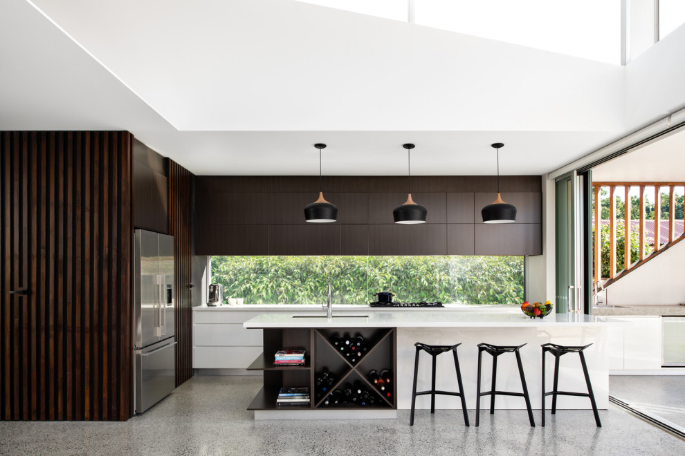 Moderne Küche in L-Form mit Unterbauwaschbecken, flächenbündigen Schrankfronten, dunklen Holzschränken, Rückwand-Fenster, Küchengeräten aus Edelstahl, Betonboden, Kücheninsel, grauem Boden und weißer Arbeitsplatte in Sydney
