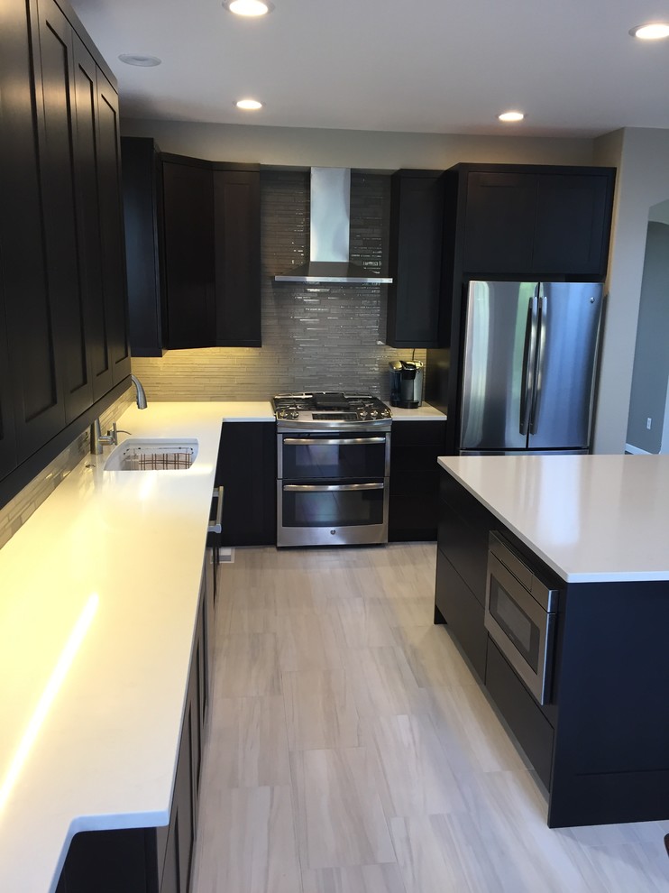 Large transitional l-shaped laminate floor and beige floor enclosed kitchen photo in Denver with an undermount sink, shaker cabinets, dark wood cabinets, solid surface countertops, gray backsplash, glass tile backsplash, stainless steel appliances and an island
