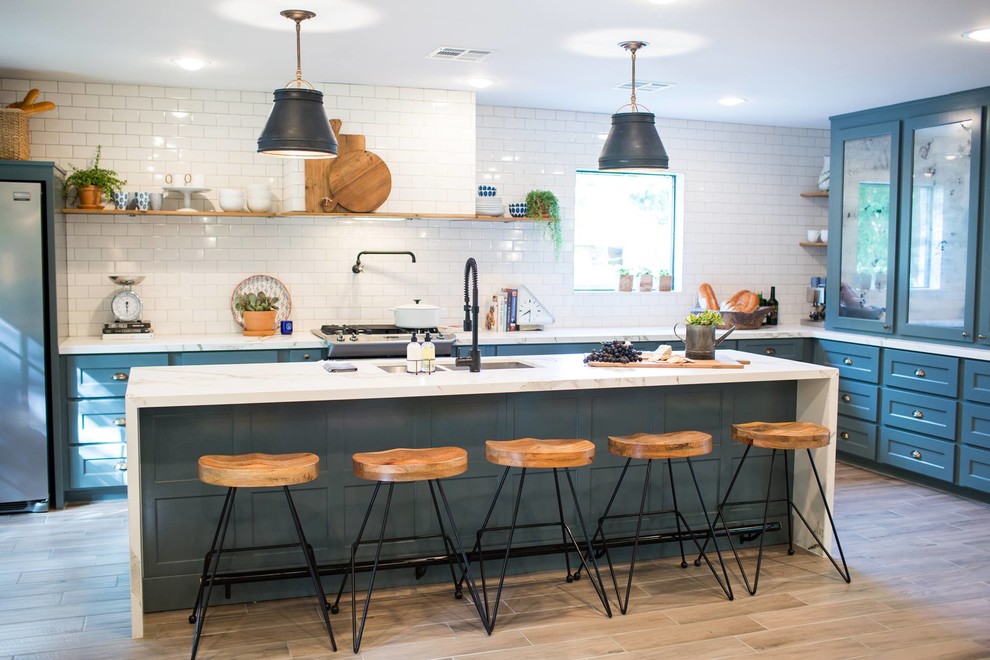This is an example of a traditional l-shaped kitchen in Austin with a submerged sink, glass-front cabinets, blue cabinets, white splashback, metro tiled splashback, light hardwood flooring and an island.