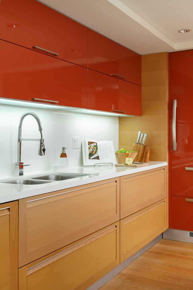 Moderne Küche mit Unterbauwaschbecken, flächenbündigen Schrankfronten, roten Schränken, Elektrogeräten mit Frontblende, braunem Holzboden, braunem Boden und weißer Arbeitsplatte in Vancouver