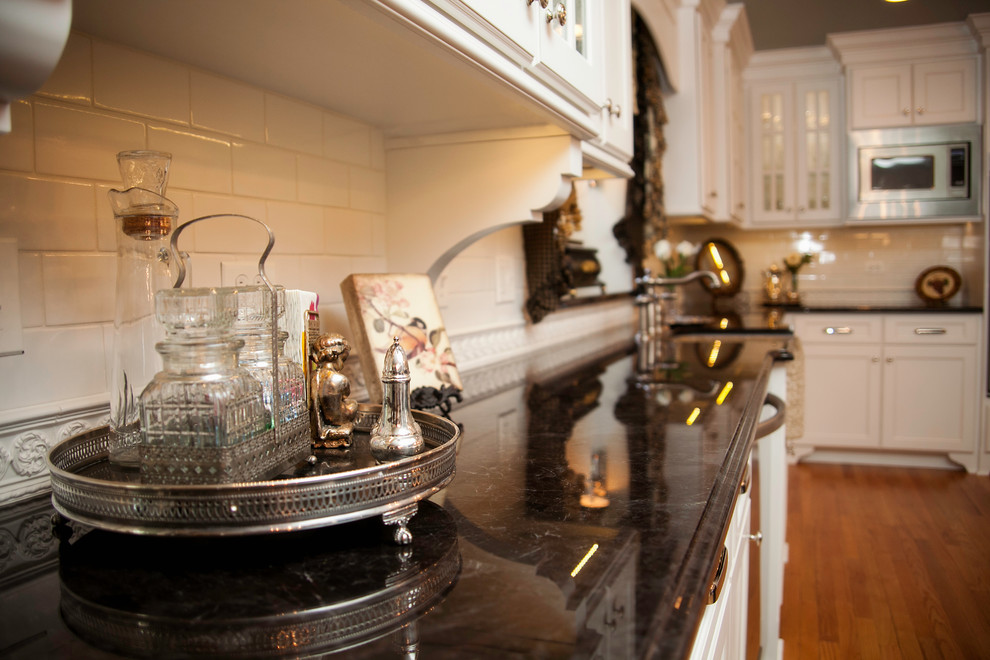 Foto på ett avskilt, stort vintage l-kök, med en rustik diskho, luckor med infälld panel, vita skåp, granitbänkskiva, vitt stänkskydd, stänkskydd i porslinskakel, rostfria vitvaror, ljust trägolv och en köksö