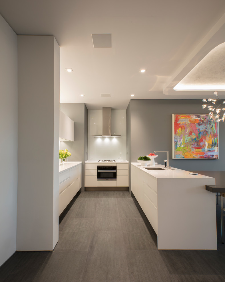 This is an example of a small modern u-shaped kitchen/diner in DC Metro with a submerged sink, flat-panel cabinets, white cabinets, white splashback, glass sheet splashback, white appliances, porcelain flooring, an island, grey floors, white worktops and quartz worktops.