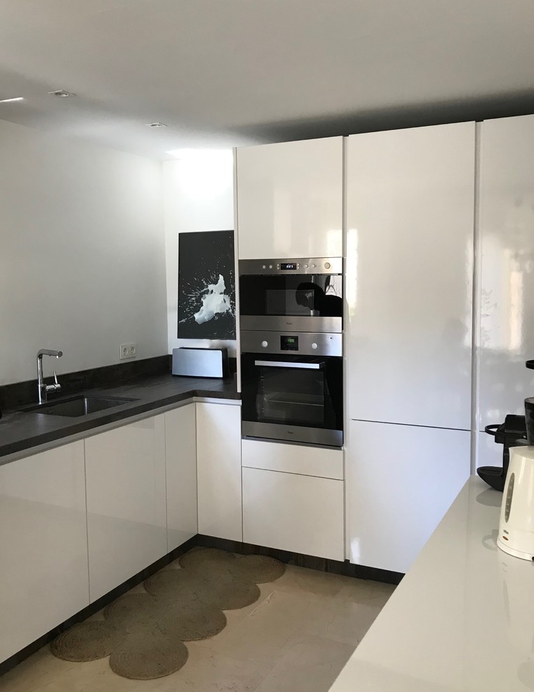 Medium sized modern l-shaped kitchen/diner in New York with a submerged sink, flat-panel cabinets, white cabinets, engineered stone countertops, brown splashback, stone slab splashback, white appliances, terrazzo flooring and beige floors.