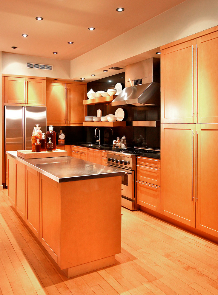 Example of a mid-sized transitional u-shaped light wood floor eat-in kitchen design in New York with shaker cabinets, light wood cabinets, stainless steel countertops, black backsplash, stainless steel appliances and an island