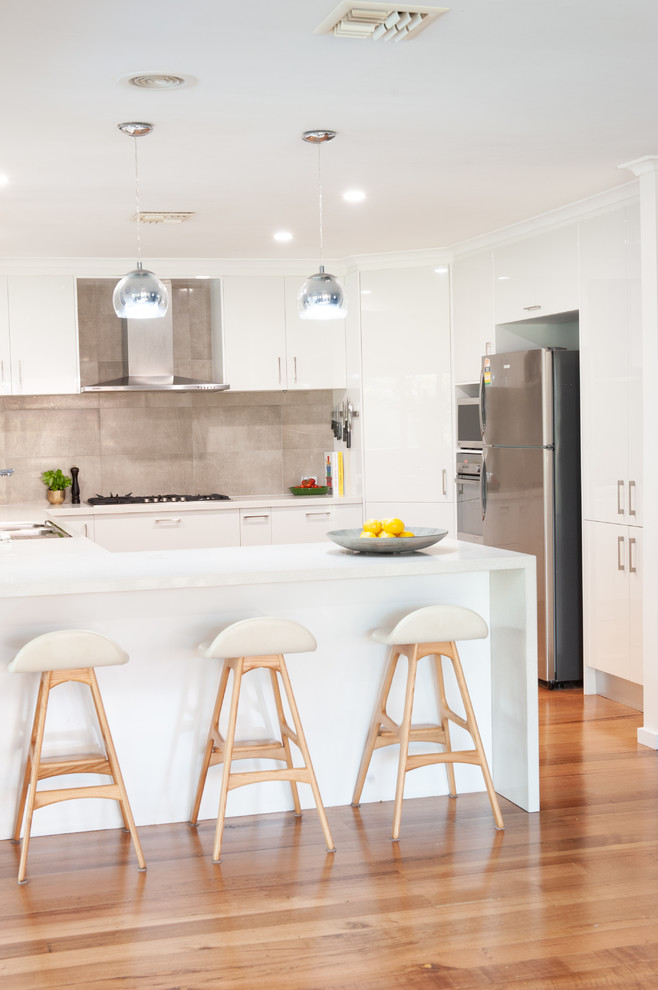 This is an example of a medium sized modern l-shaped kitchen in Melbourne with a double-bowl sink, open cabinets, white cabinets, composite countertops, white splashback, stone tiled splashback, stainless steel appliances, medium hardwood flooring, an island and white worktops.