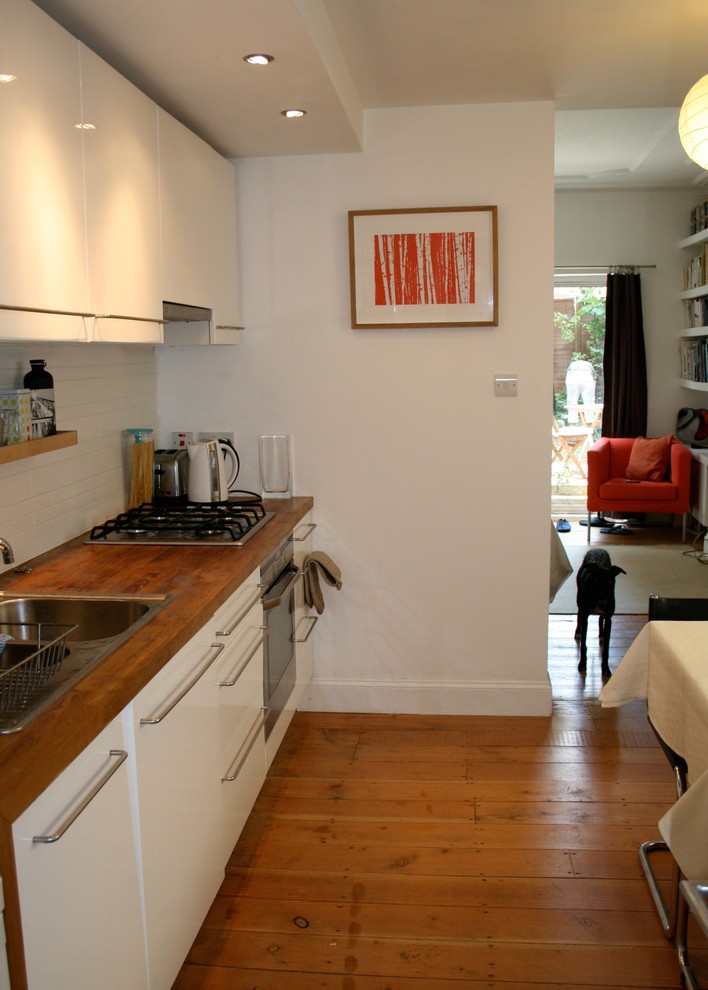 Exempel på ett litet minimalistiskt kök, med en enkel diskho, släta luckor, vita skåp, träbänkskiva, vitt stänkskydd, stänkskydd i keramik och rostfria vitvaror