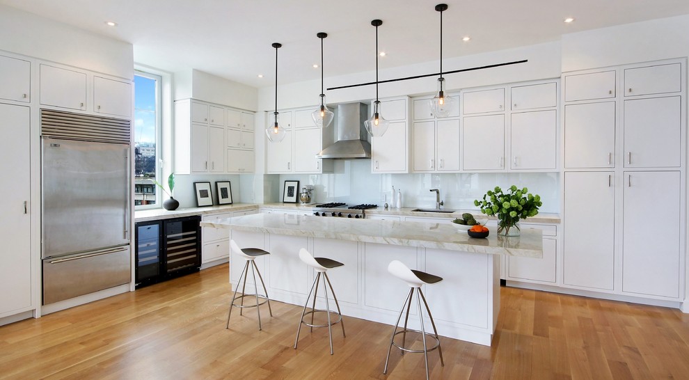 Bild på ett funkis grå grått kök, med en undermonterad diskho, släta luckor, vita skåp, vitt stänkskydd, glaspanel som stänkskydd, rostfria vitvaror, mellanmörkt trägolv, en köksö och brunt golv