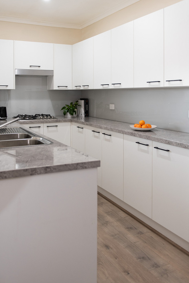 Bild på ett litet funkis grå grått kök, med en dubbel diskho, öppna hyllor, vita skåp, laminatbänkskiva, grått stänkskydd, glaspanel som stänkskydd, rostfria vitvaror och ljust trägolv
