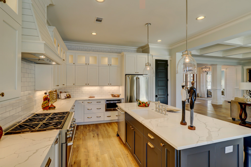 Inspiration for a large farmhouse l-shaped open plan kitchen in Atlanta with a submerged sink, shaker cabinets, white cabinets, engineered stone countertops, white splashback, metro tiled splashback, stainless steel appliances, light hardwood flooring, an island, brown floors and white worktops.