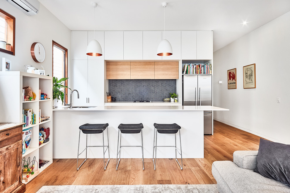 Exemple d'une cuisine ouverte parallèle tendance avec un évier 2 bacs, un placard à porte plane, des portes de placard blanches, une crédence grise, un électroménager en acier inoxydable, un sol en bois brun et une péninsule.