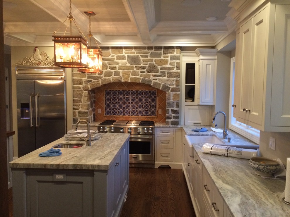 Large traditional l-shaped kitchen/diner in Philadelphia with a belfast sink, shaker cabinets, white cabinets, composite countertops, terracotta splashback, stainless steel appliances, medium hardwood flooring and multiple islands.