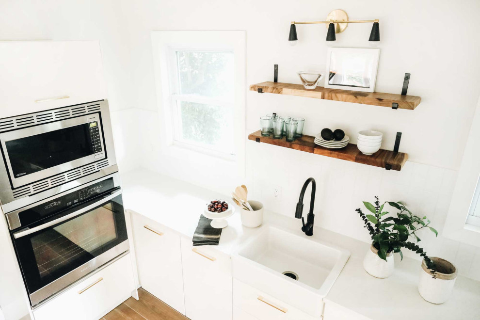 Example of a small trendy galley ceramic tile and brown floor eat-in kitchen design in Other with a farmhouse sink, flat-panel cabinets, white cabinets, quartz countertops, white backsplash, subway tile backsplash, stainless steel appliances, an island and white countertops