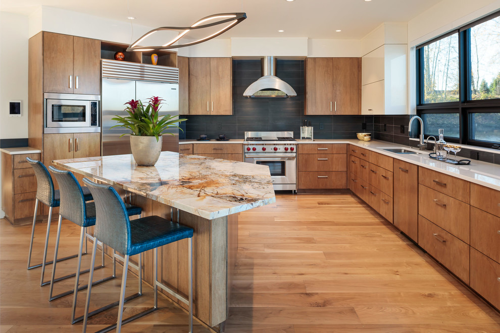 Moderne Küche in L-Form mit Unterbauwaschbecken, flächenbündigen Schrankfronten, hellbraunen Holzschränken, Küchenrückwand in Schwarz, Küchengeräten aus Edelstahl, braunem Holzboden, Kücheninsel, braunem Boden und weißer Arbeitsplatte in Portland