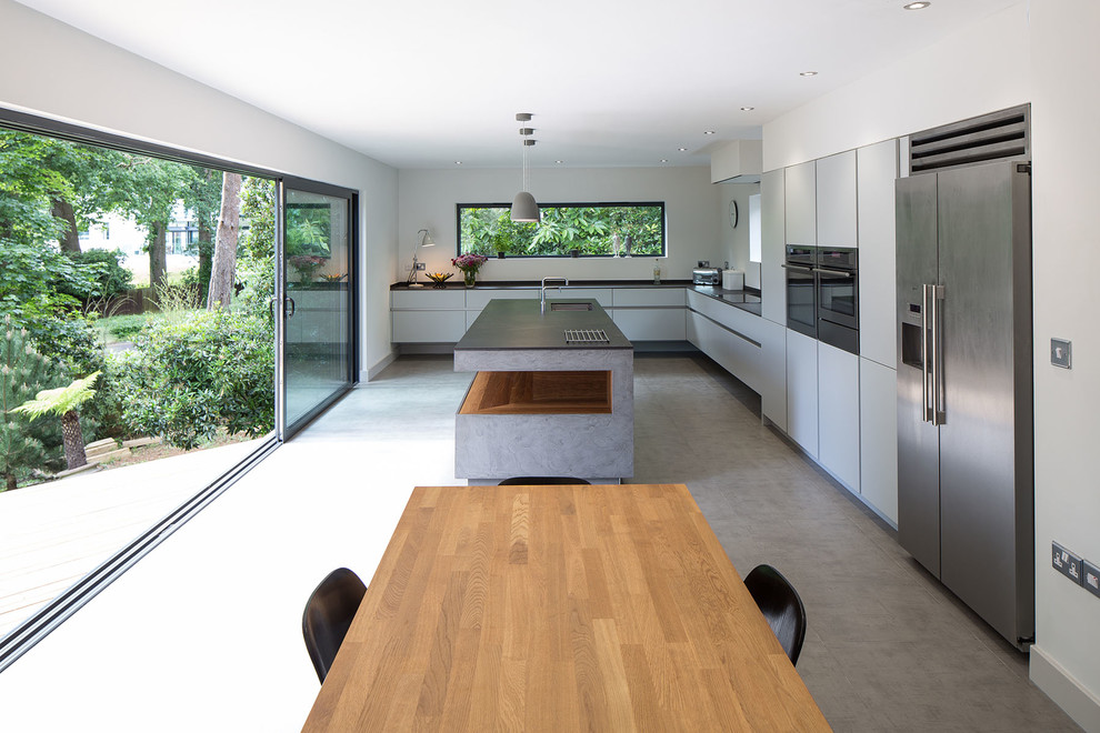 Kleine Moderne Wohnküche in L-Form mit Unterbauwaschbecken, flächenbündigen Schrankfronten, grauen Schränken, Küchenrückwand in Weiß, Küchengeräten aus Edelstahl, Betonboden, Kücheninsel und grauem Boden in Dorset