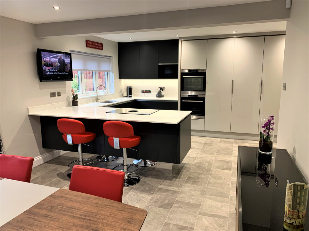 This is an example of a medium sized contemporary u-shaped kitchen/diner in Other with a submerged sink, flat-panel cabinets, grey cabinets, black appliances, vinyl flooring, a breakfast bar and grey floors.