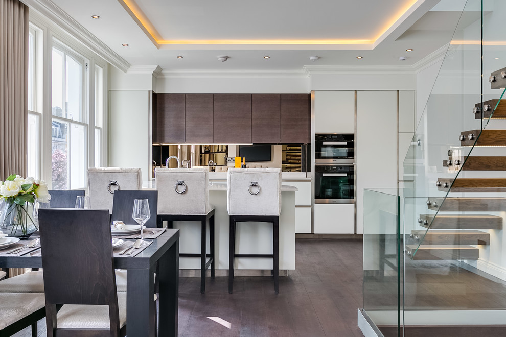 Inspiration for a contemporary galley kitchen/diner in London with flat-panel cabinets, white cabinets, mirror splashback, integrated appliances, medium hardwood flooring, an island, brown floors and white worktops.