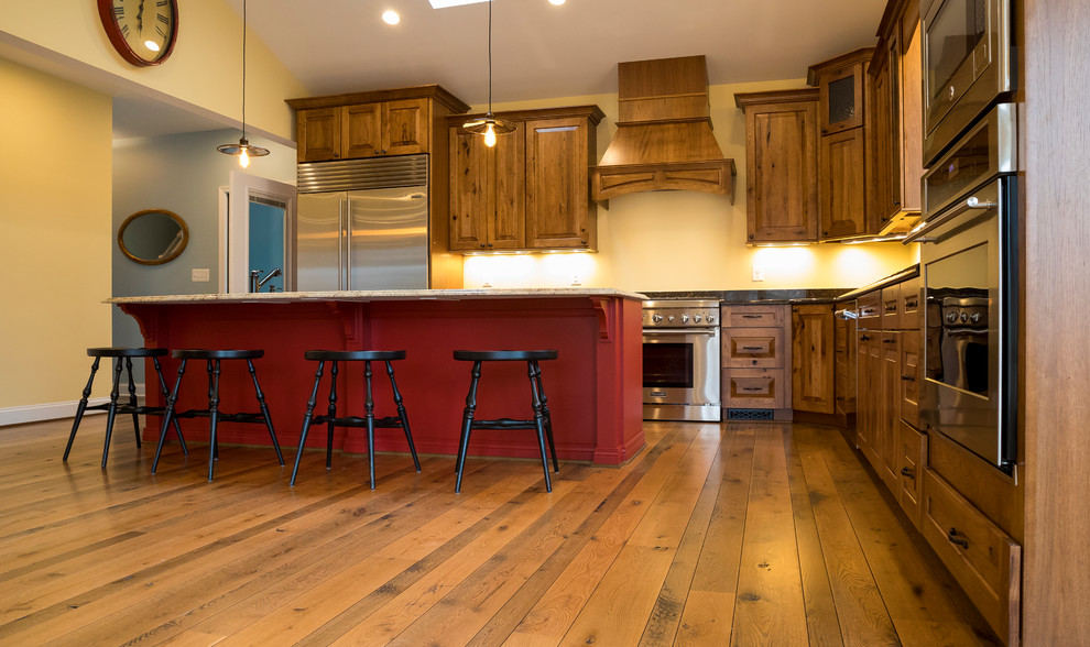 Foto på ett stort vintage kök, med rostfria vitvaror, en köksö, en undermonterad diskho, luckor med upphöjd panel, skåp i mellenmörkt trä, granitbänkskiva, mellanmörkt trägolv och brunt golv